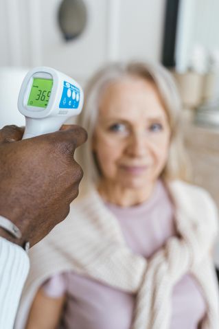 Nurse checks temperature of senior woman using an infrared thermometer.
